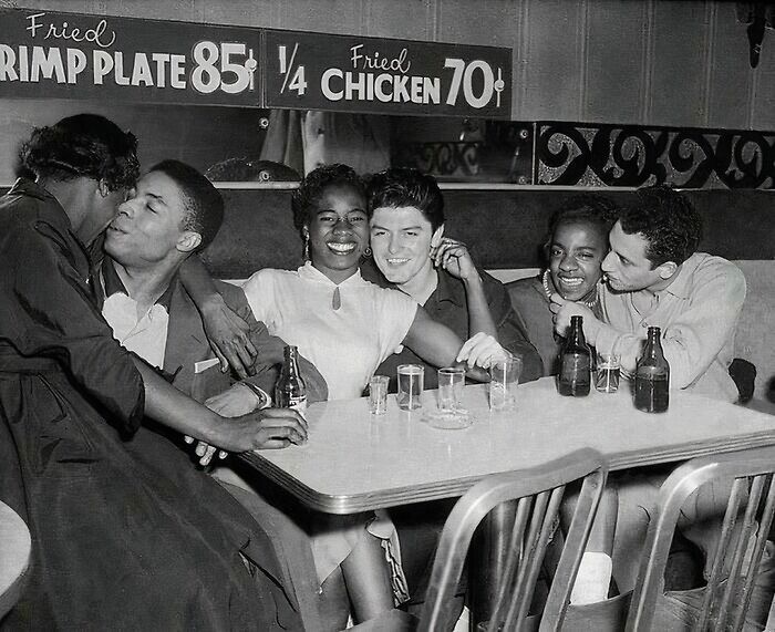 Group of friends enjoying time at a diner, with vintage pricing signs in the background, showcasing rare historical moments.