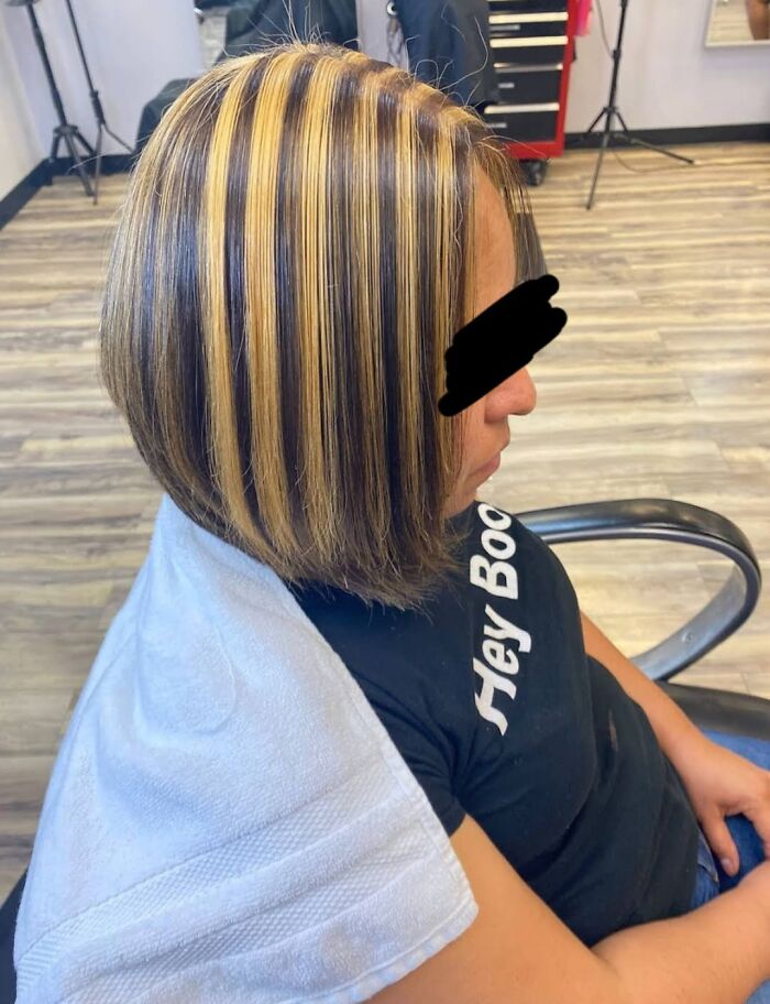 Hair fail with uneven striped highlights, woman sitting in a salon chair, wearing a black shirt and blue jeans.