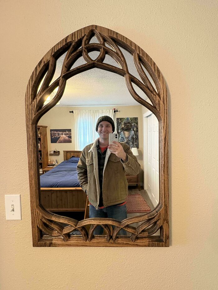 Man taking a mirror selfie framed by intricate woodworking project, showcasing impressive craftsmanship.