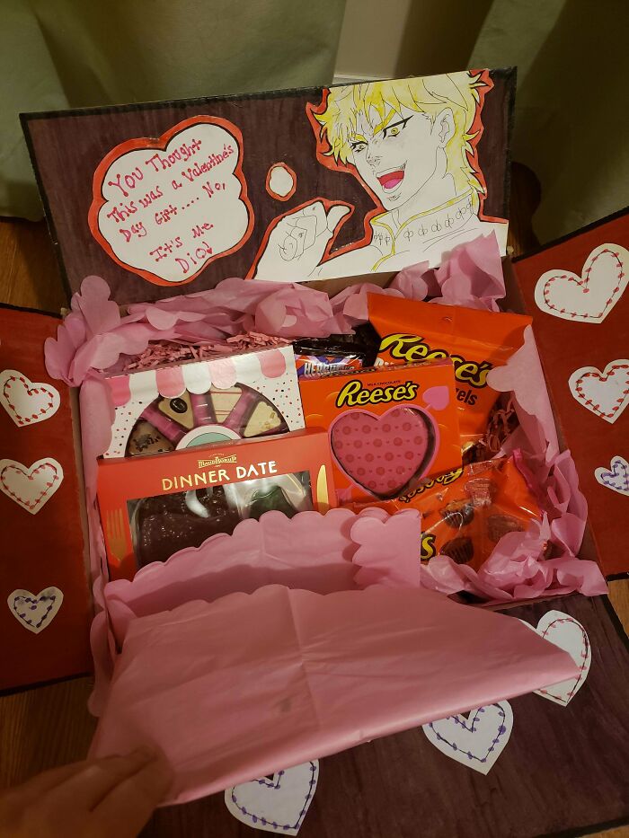 Valentine's Day gift box with chocolates, Reese's, and a humorous anime card decorated with hearts.