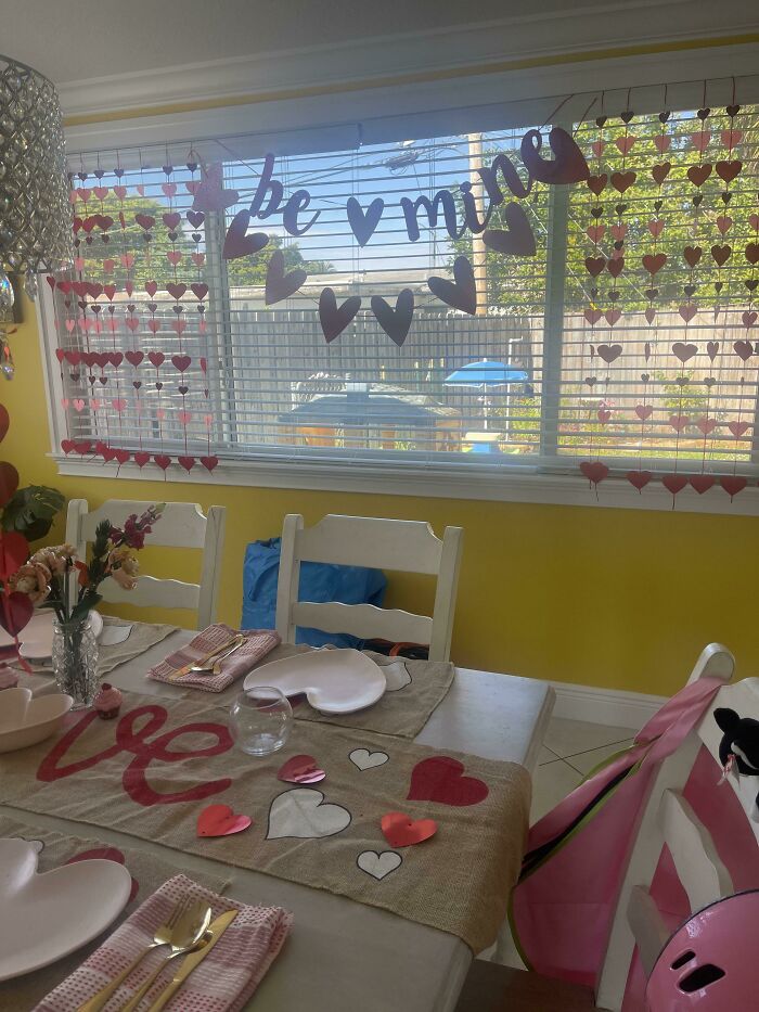 Valentine's Day-themed table setting with heart decorations and "be mine" window banner.