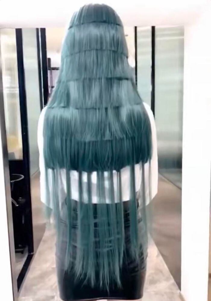 Long, uneven layered green hair from behind, showcasing a hair fail in an office hallway.