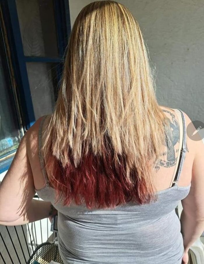 Woman with long, uneven hair, showing a hair fail with mismatched blonde and red dye, wearing a gray tank top.