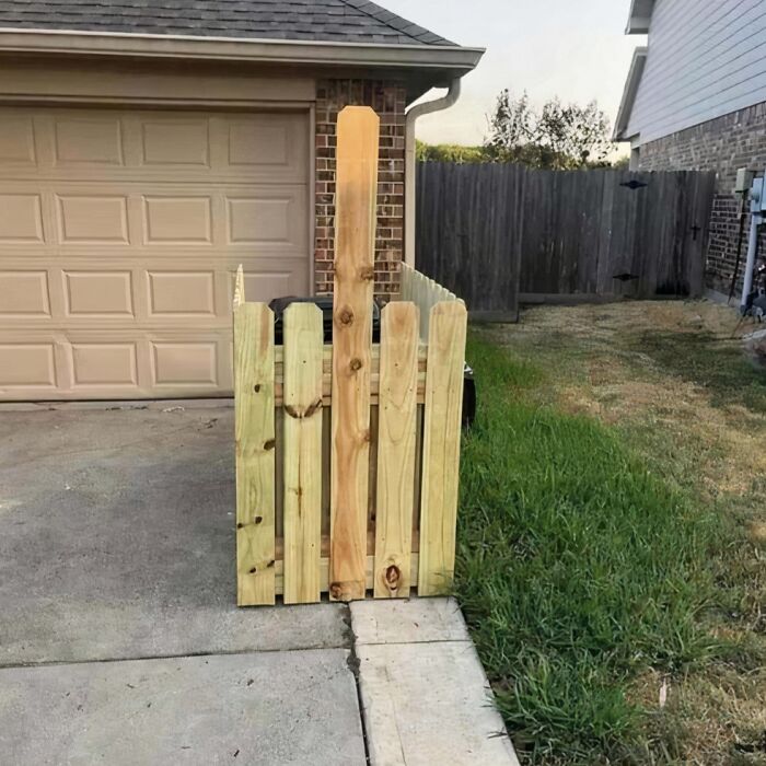 Unique garden fence with uneven planks on a driveway near a garage.