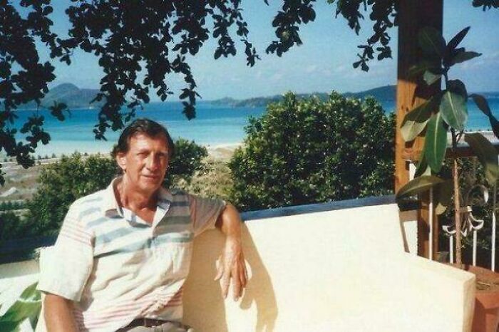 Man sitting on a bench overlooking a scenic beach view, with greenery and ocean in background, sharing interesting facts.