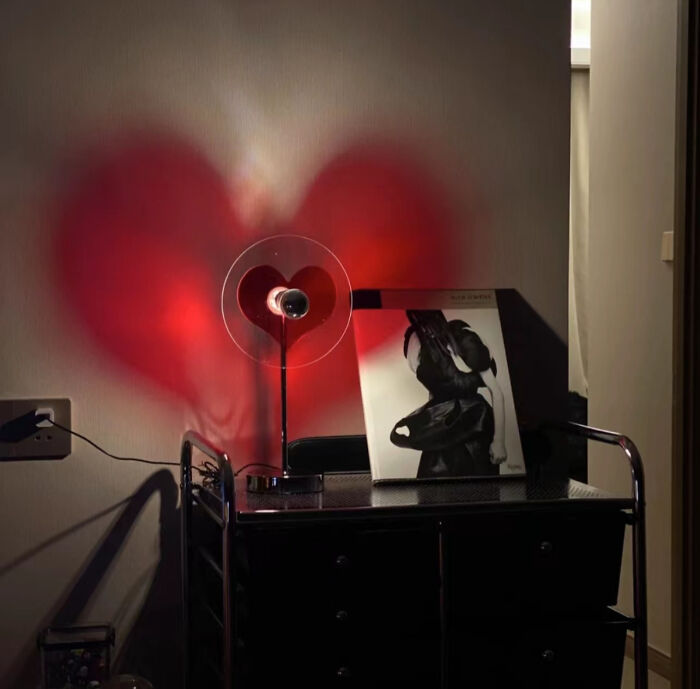 Heart-shaped red light on wall next to a stylish lamp and art print, perfect inspiration for Valentine's Day gifts.