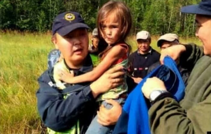 Rescue team member holds a child in a grassy field, while others assist, highlighting interesting facts of human resilience.