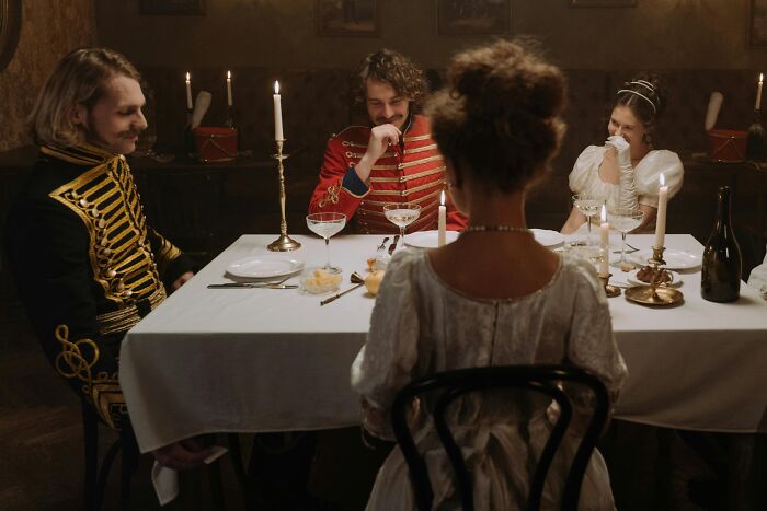 Victorian-era dinner party scene with four people, creating a mic-drop moment in a dimly lit room with candles.