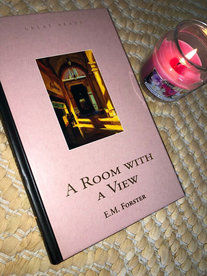 Romantic book "A Room with a View" by E.M. Forster next to a pink candle on a woven surface.