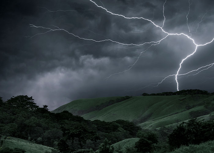 Stormy landscape with lightning striking above a forested hill, evoking a sense of scary and treacherous hiking conditions.