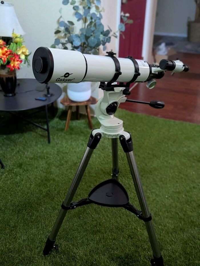 Telescope on a tripod in a room with plants and furniture, highlighting spending money on quality stargazing equipment.