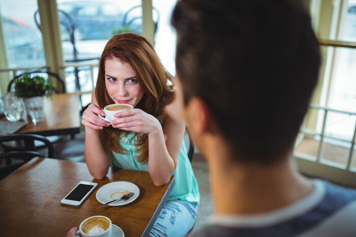 Woman holding a coffee cup, looking unimpressed on a first date in a cozy cafe setting.