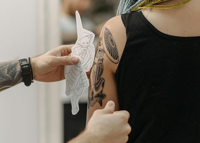 Person holding tattoo design next to inked arm in a studio setting.