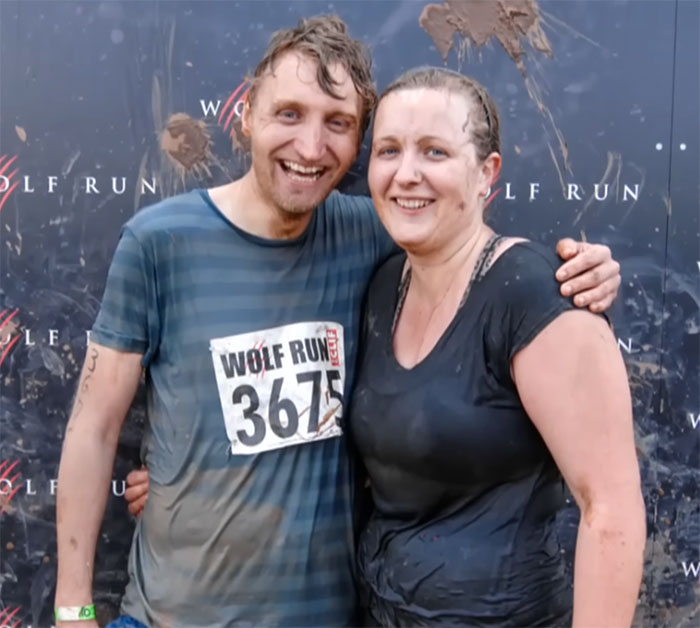 Participants at Wolf Run event, muddy and smiling, against dark backdrop.