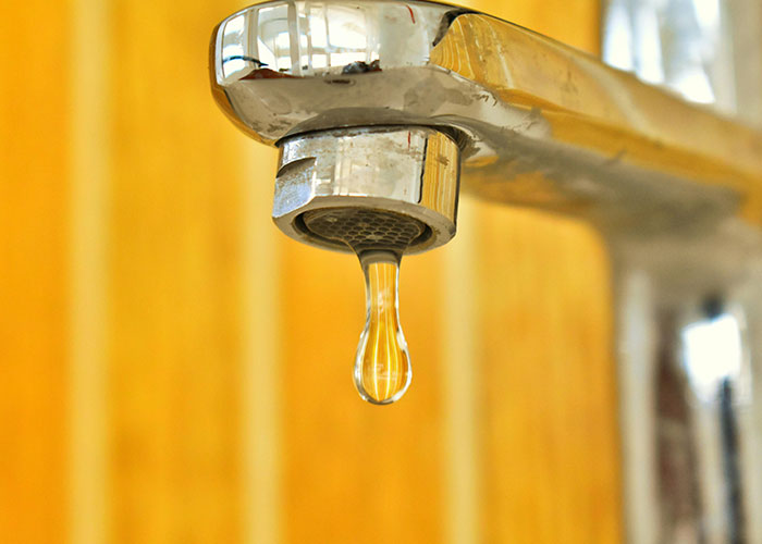 Close-up of a dripping faucet with a wooden background, highlighting a common Europe culture shock for Americans.