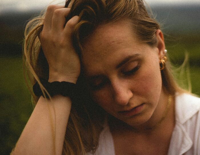 Woman with a somber expression, hand in hair.