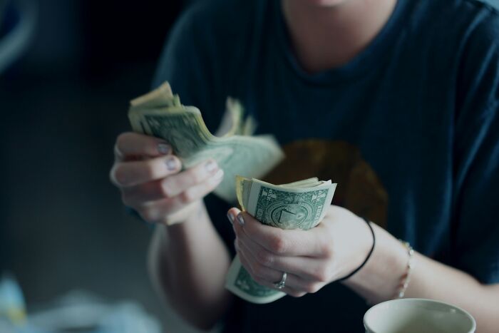 Person counting dollar bills while sitting at a table.