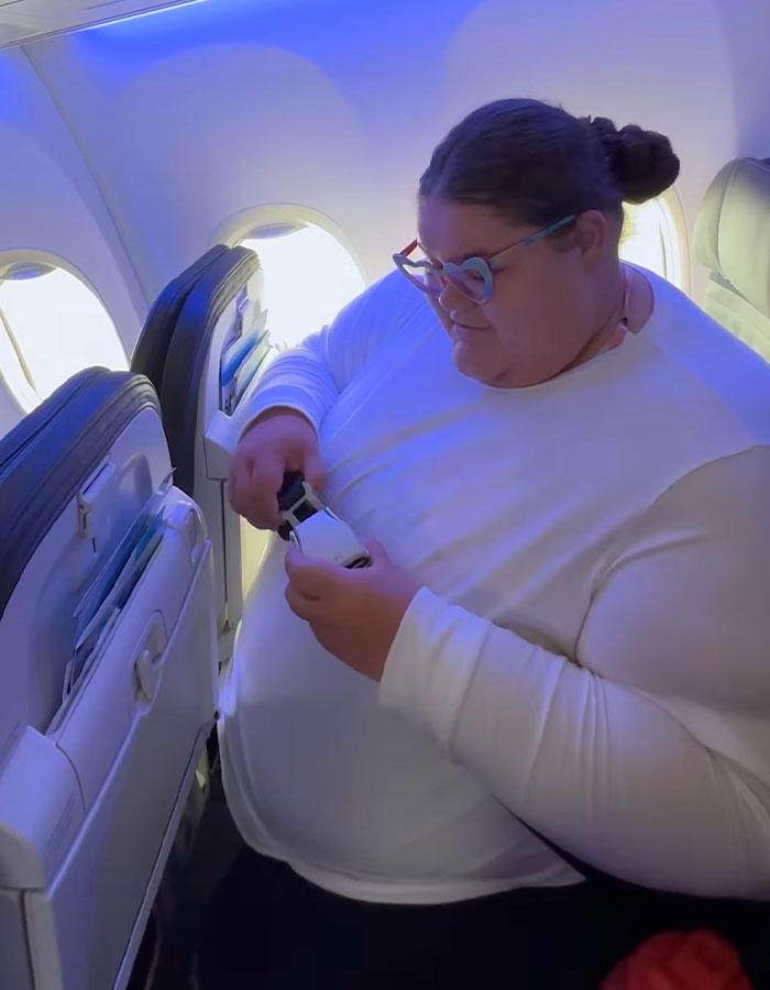 Passenger on a flight adjusting seatbelt, highlighting the debate on airline discrimination against obese passengers.