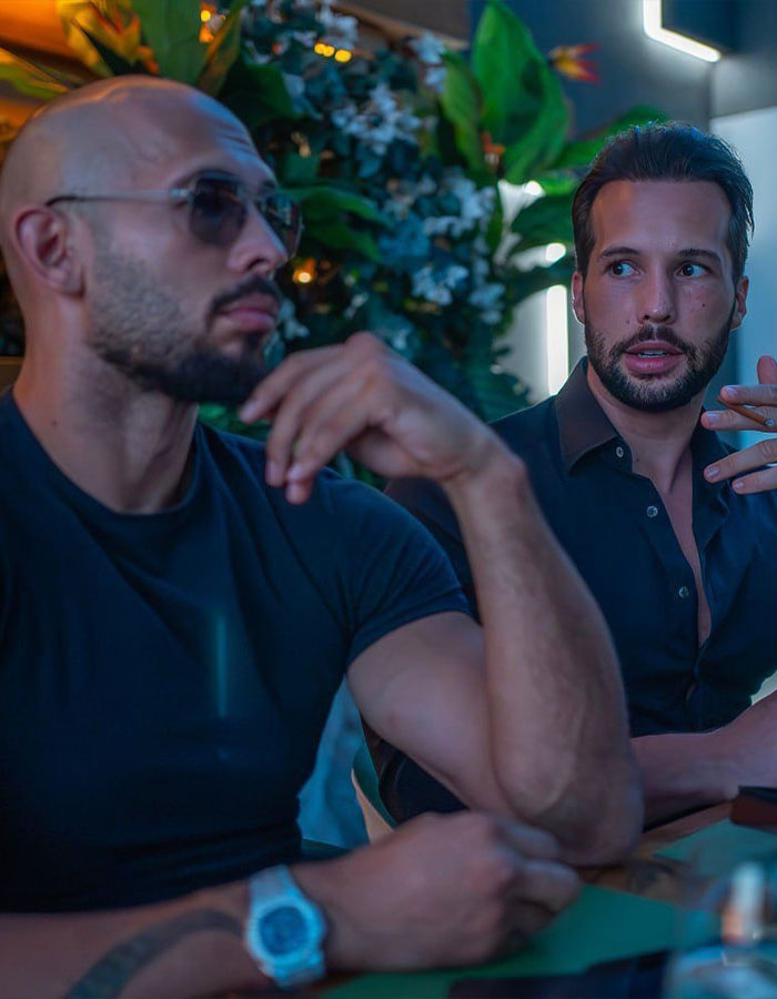 Two men in conversation, one wearing sunglasses, indoors with greenery background, related to trafficking charges.