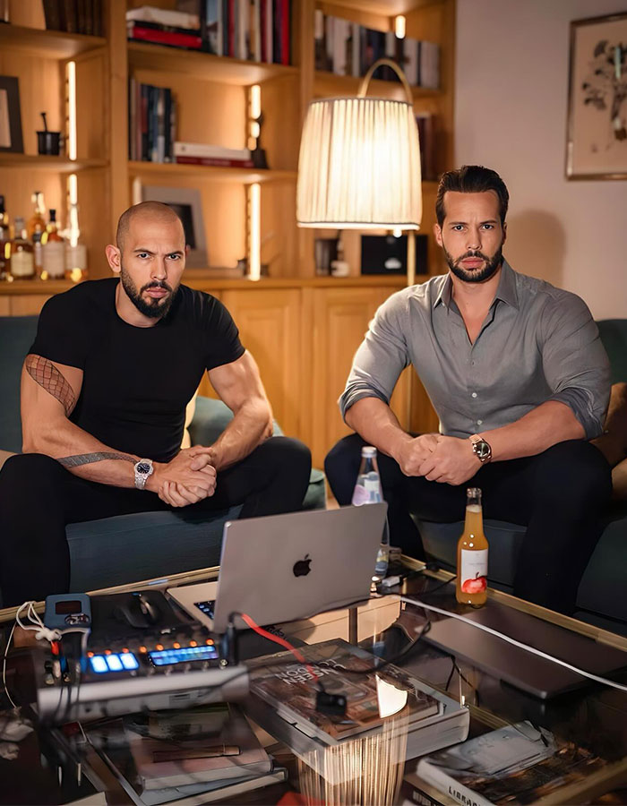 Two men sitting in a living room with a laptop on a table, discussing trafficking charges.