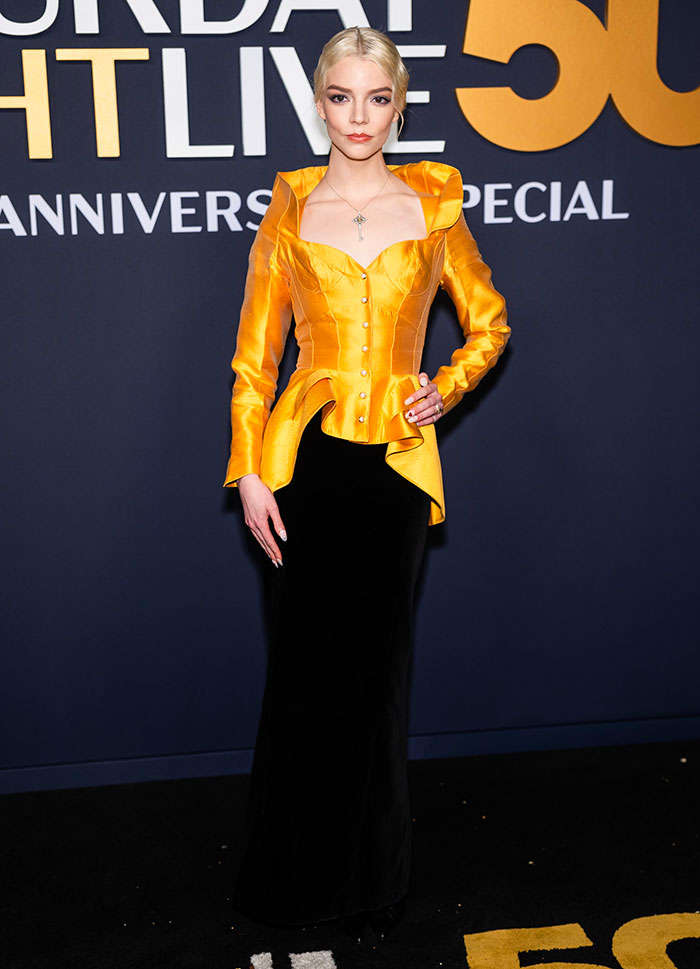 Person in a striking yellow and black outfit on the SNL 50th Anniversary red carpet, showcasing a unique fashion choice.