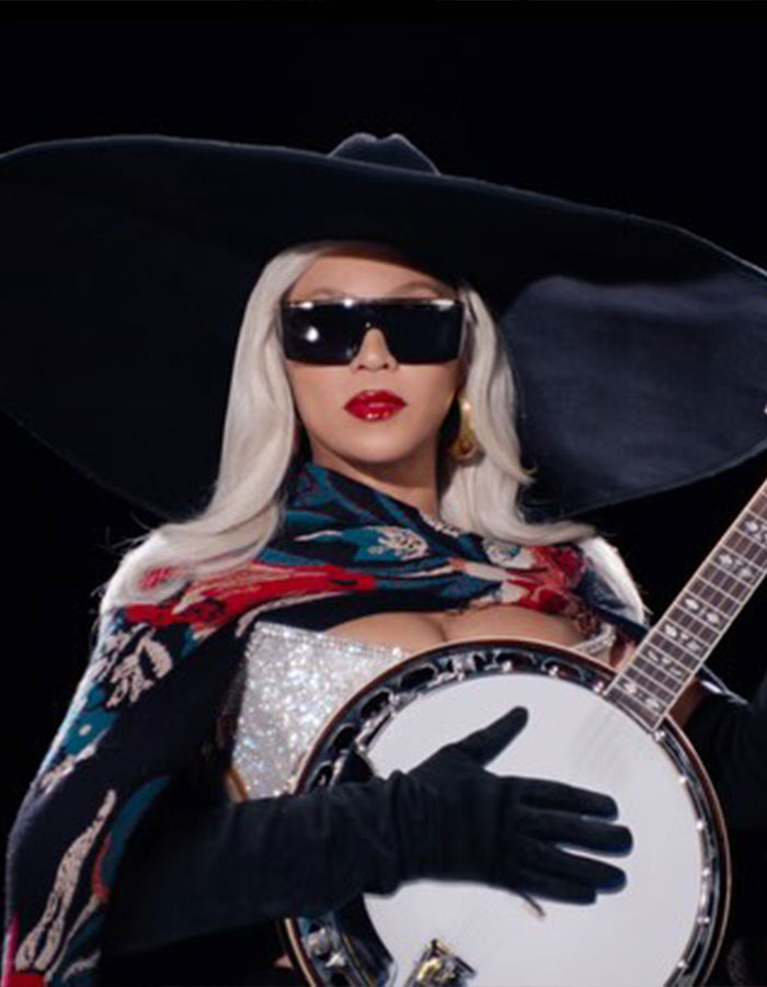 Black hat and sunglasses, person with lighter skin tone, holding a banjo at an event.