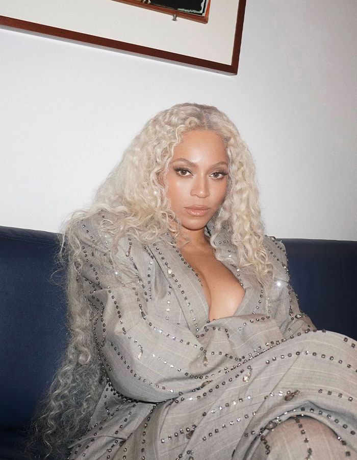 Woman with blonde hair in a studded beige outfit, sitting on a couch, related to a skin tone debate at the Grammys.