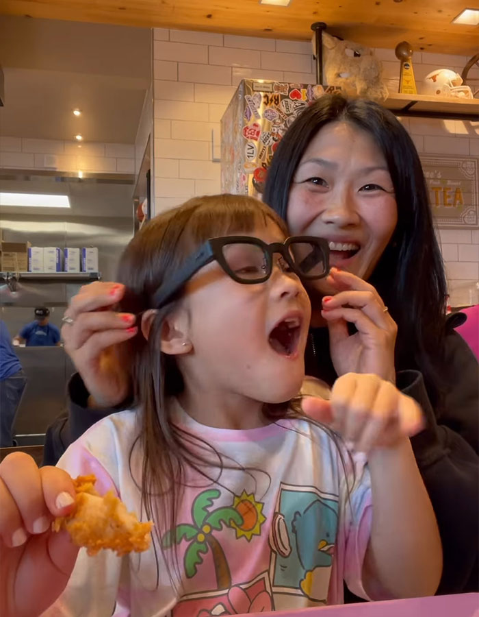 Deaf girl, age 10, experiences spoken words through glasses, joyful reaction with woman in a vibrant setting.