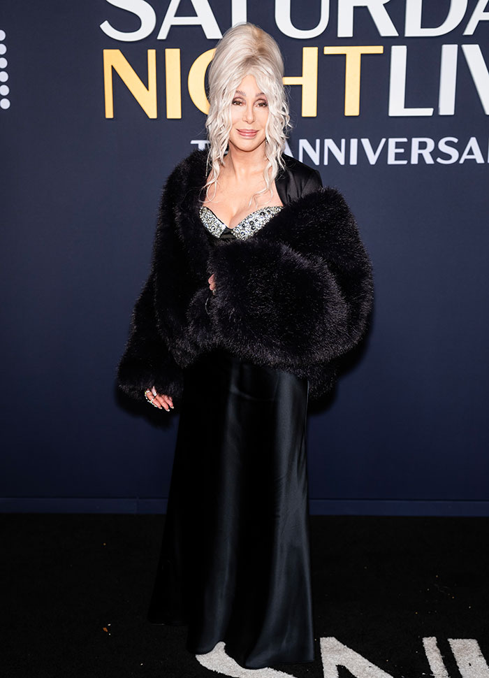 Person on SNL 50th red carpet in a glamorous black gown and fur wrap.