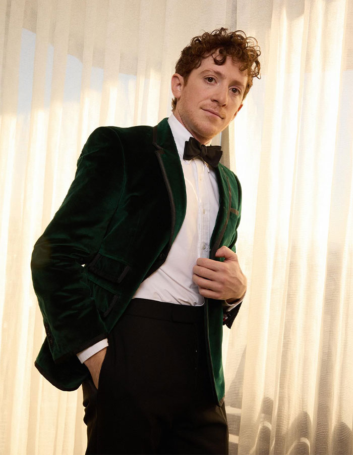 A person in a green velvet suit at the Critics Choice Awards standing by a curtain, creating a stylish appearance.