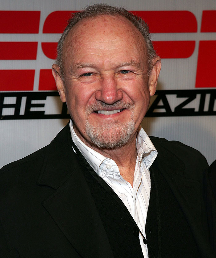 Hollywood legend smiling in a formal setting, wearing a black jacket and white shirt.