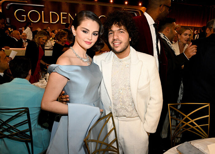 A woman in an elegant blue gown and a man in a white suit at a formal event, sparking conversation among fans.