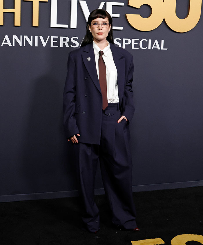 Person in oversized navy suit at SNL 50th anniversary red carpet event.