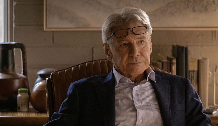 Elderly man in a blazer with glasses, seated indoors, featuring books in the background, related to a stroke patient theme.