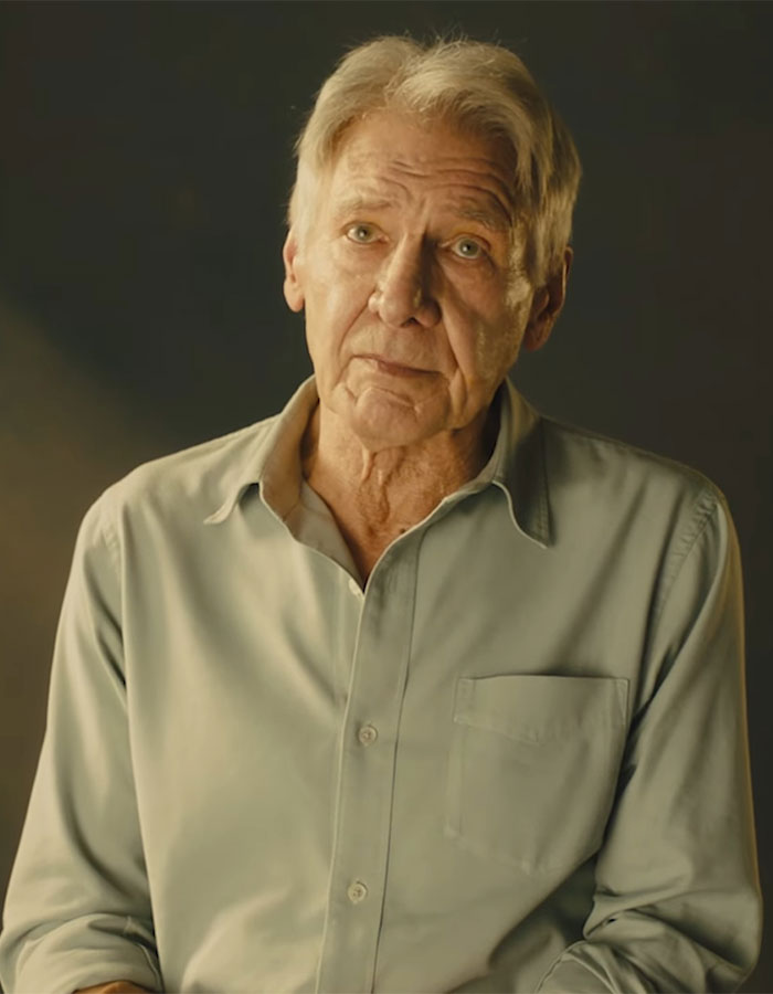 Elderly man in a beige shirt poses against a dark background, conveying serious expression.