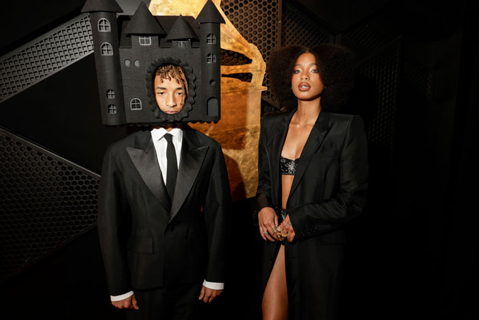 Young man in a castle-themed outfit and woman in a black suit at the Grammys 2025.