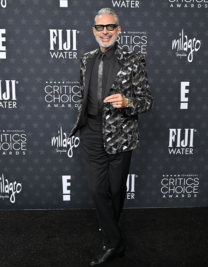 Celebrity in daring outfit at Critics Choice Awards red carpet, wearing a patterned blazer and sunglasses, posing confidently.