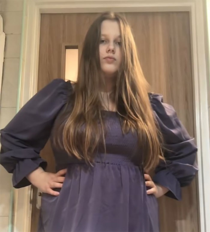 Young woman in a blue dress stands confidently in front of a wooden door.