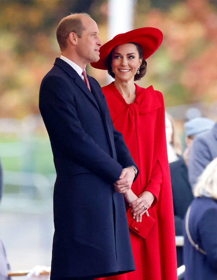 Royal couple at an event; Kate Middleton in a striking red outfit, showcasing her fashion policy amidst recent debates.