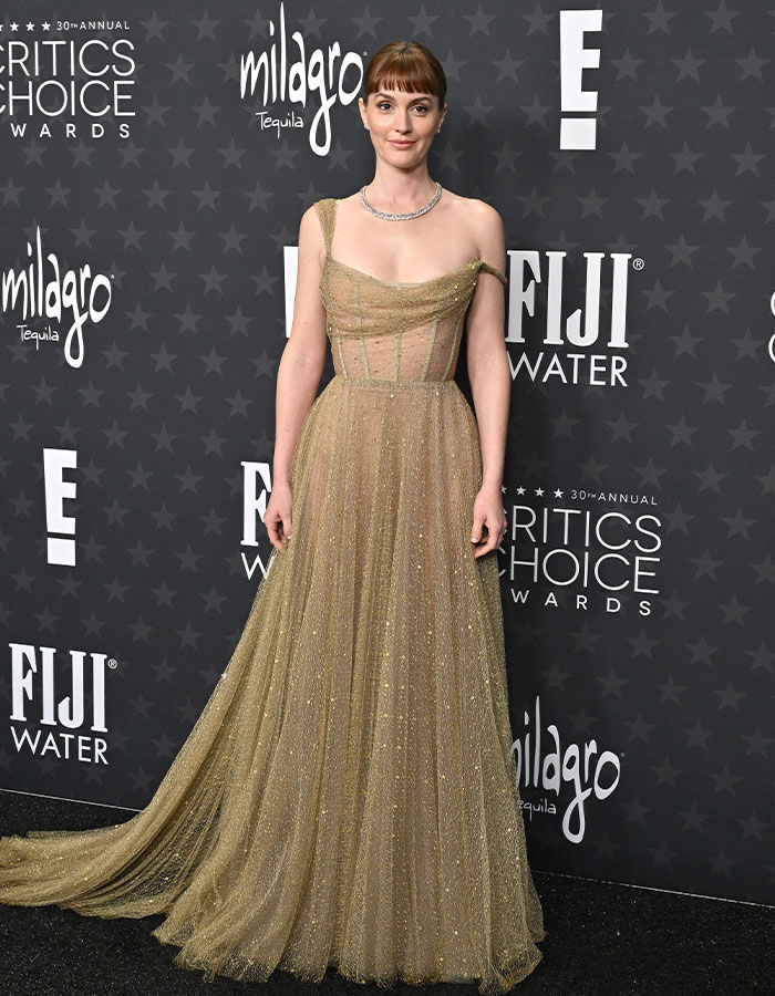 Person in a shimmering gold gown at Critics Choice Awards red carpet.