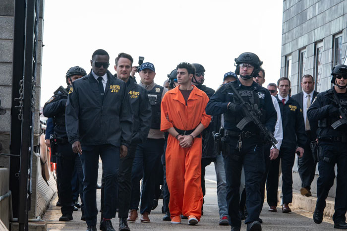 Person in an orange jumpsuit escorted by security, related to Luigi Mangione public statement.