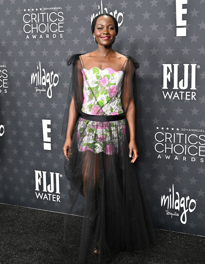 Woman in a floral dress with sheer overlay at the Critics Choice Awards red carpet.