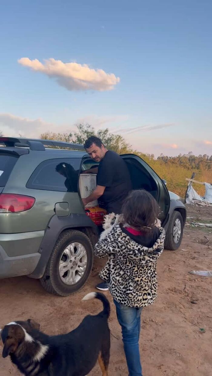 Man feeding stray dogs from SUV, joined by a child in a leopard print coat.