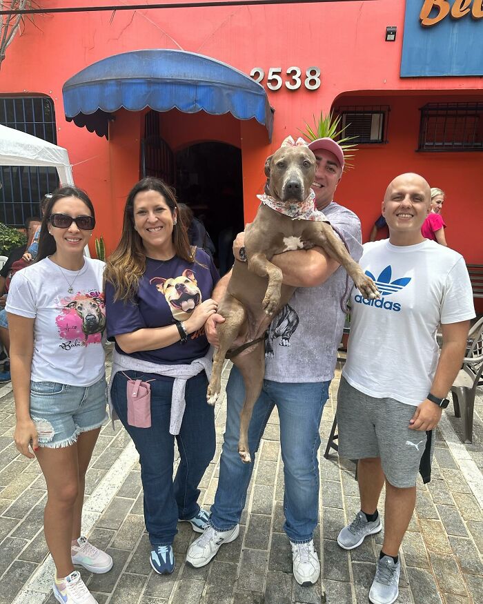 Group of people smiling with a rescued Pit Bull dog outside an orange building.