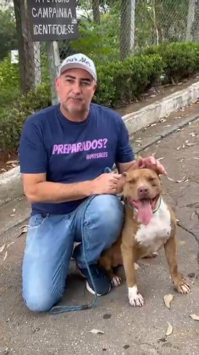 Man kneeling with a smiling Pit Bull in an outdoor setting, supporting pit bull rescue efforts.