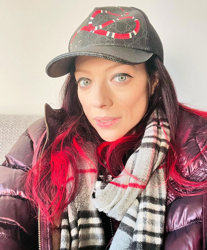 Person with red highlights wearing a Gucci cap and plaid scarf.