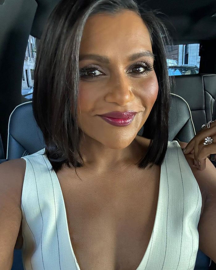 Mindy Kaling showcasing slim figure at a movie premiere, wearing a white dress and smiling in a car.