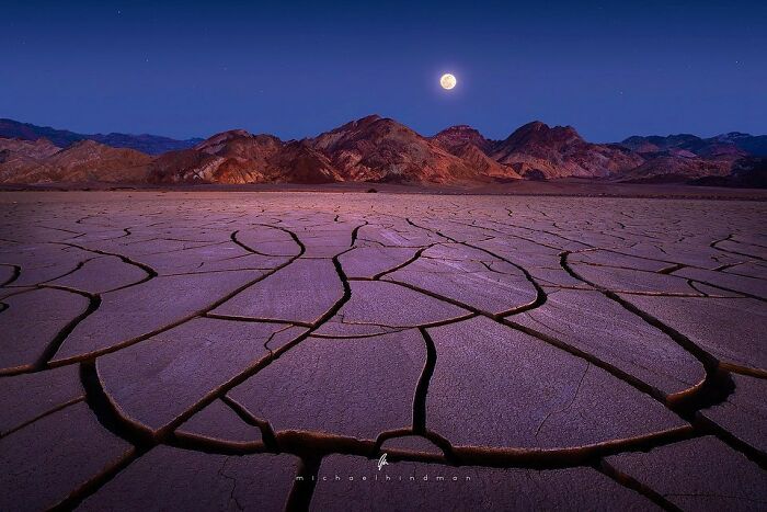 Cracked earth under moonlight, highlighting nature's textures near rugged mountains.