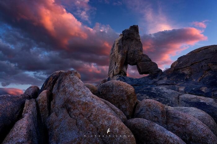 Rock formation with natural arch against a vibrant sunset sky, highlighting the textures of nature by Michael Hindman.