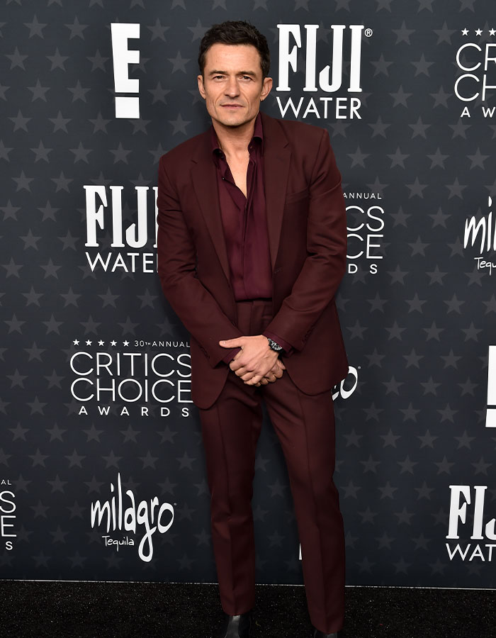 Man in a burgundy suit at Critics Choice Awards red carpet.